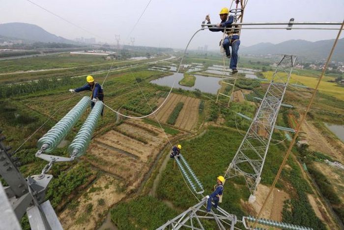 Workers install cables on a electricity pylon above crop fields in Xihu township of Tongling