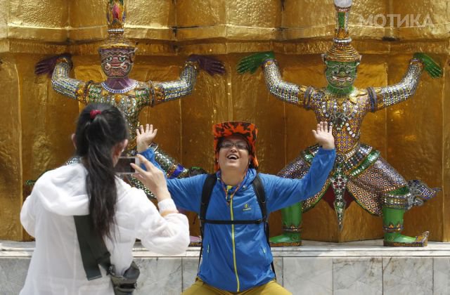 A Chinese tourist strikes a similar pose to statues as they visit the Grand Palace in Bangkok