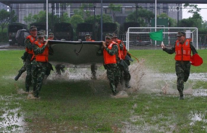 Paramilitary policemen carrying a boat run across flooded grassland as another fellow policeman guides them with flags during a drill at a military base in Suining